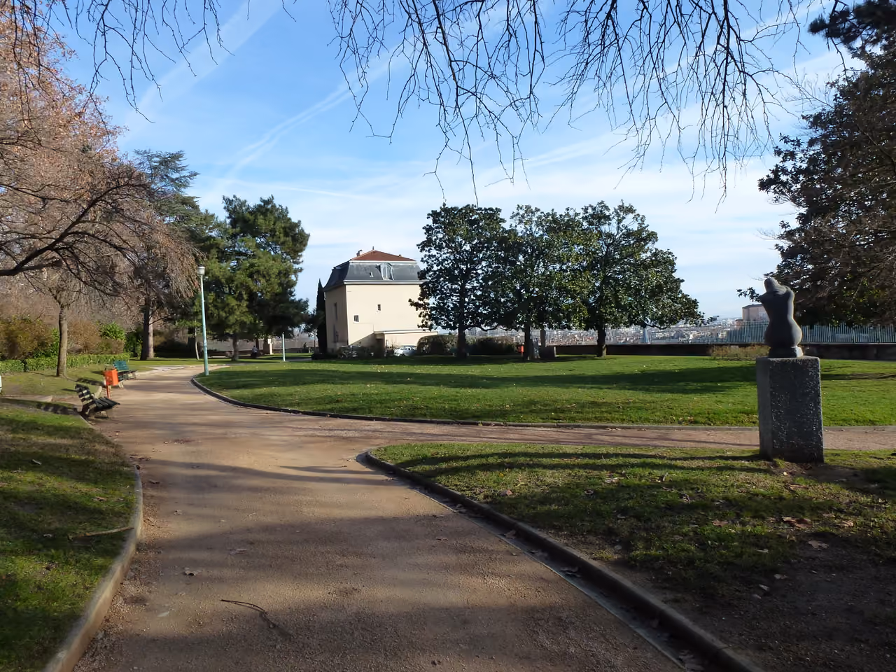 Pathway through the Jardin des Chartreux public park featuring trees, a green lawn and a sculpture