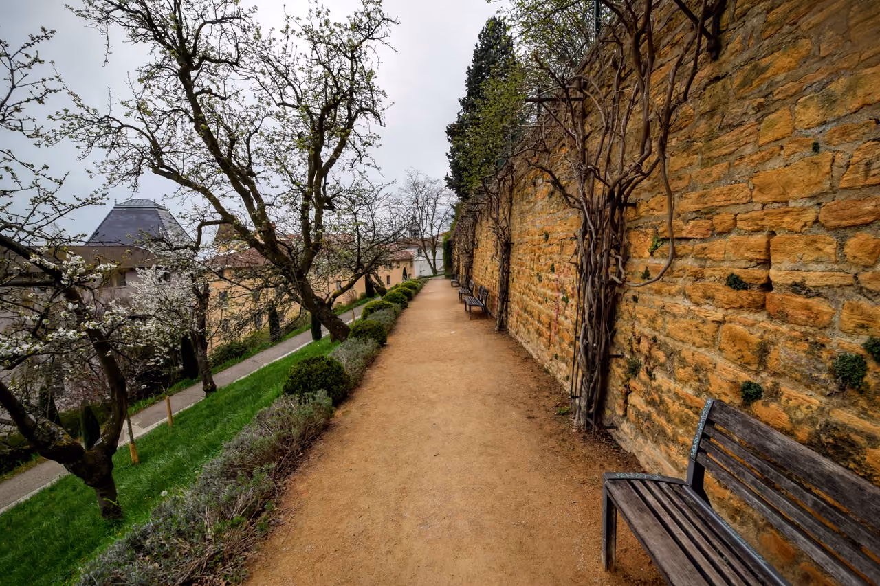 Scenic walking path lined with wooden benches and an old stone wall in the Garden of the Rosary on Fourviere Hill
