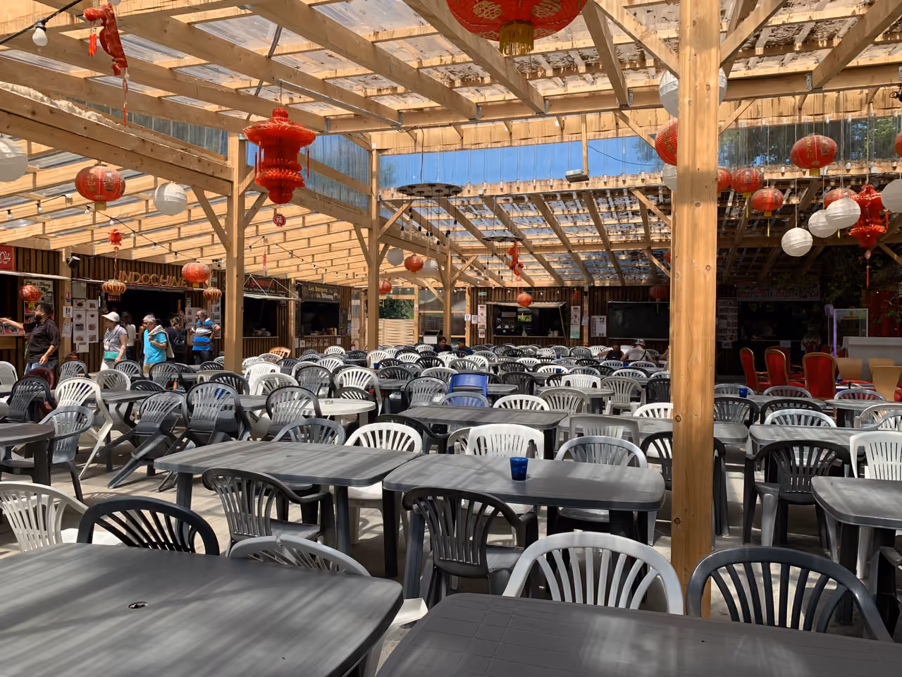 Outdoor dining area under a wooden pergola decorated with red and white lanterns at Mekong Asian Village