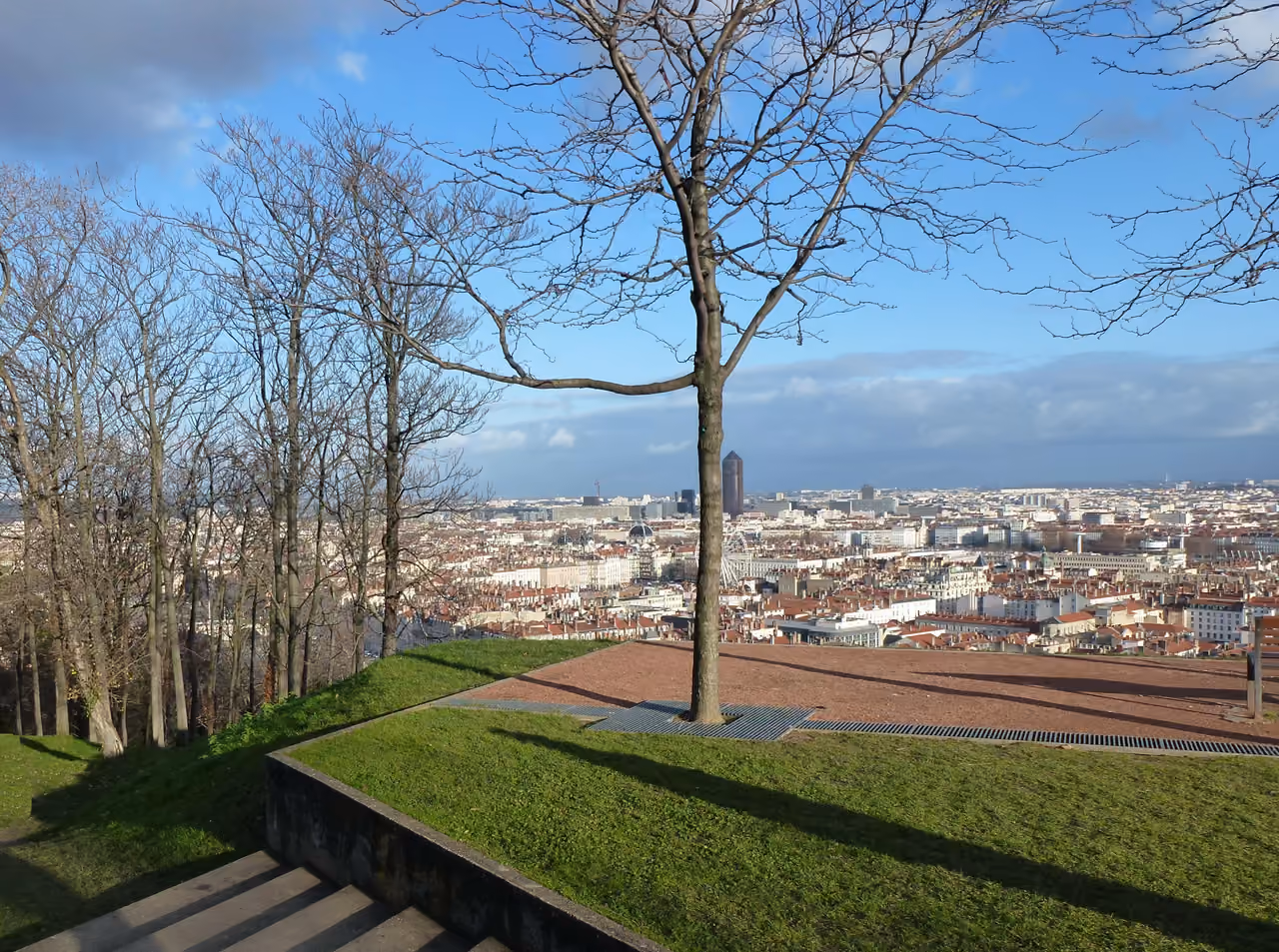 Panoramic view of a cityscape from a grassy hilltop terrace at Jardin des Curiosités