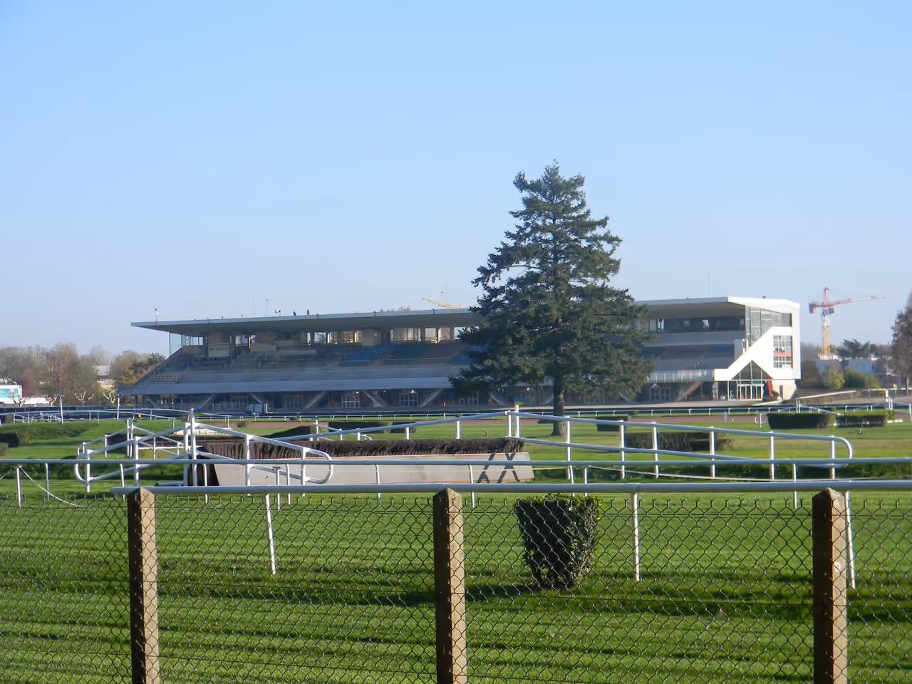 Grandstand at Parilly racecourse with green grass tracks and hurdles behind a wire fence