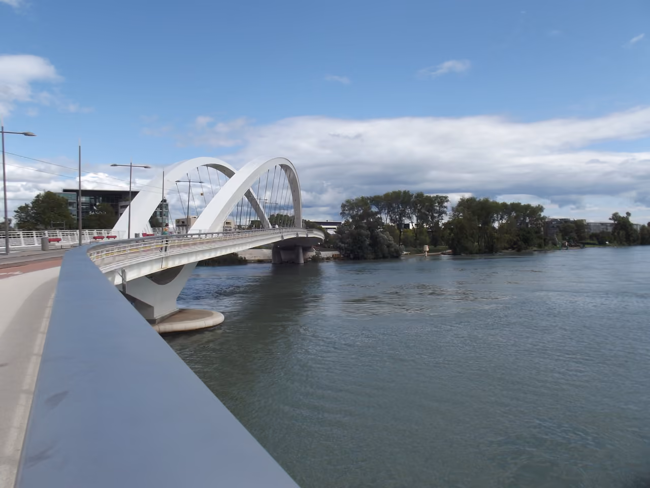 Raymond Barre Bridge with white arches over the Rhone River under a partly cloudy sky