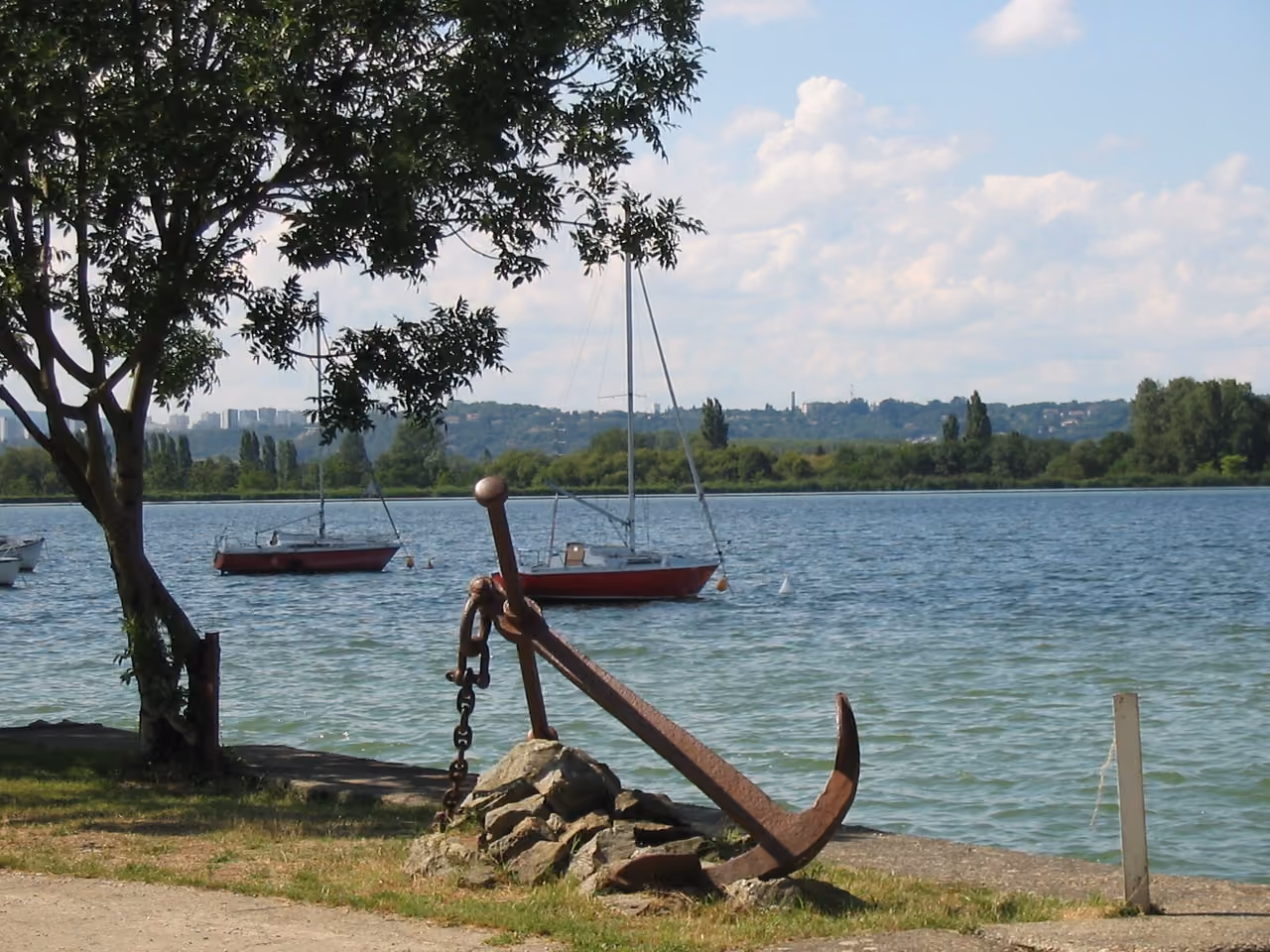 Scenic view of a rusty anchor on the shore of Le Grand Large lake with sailboats in the background