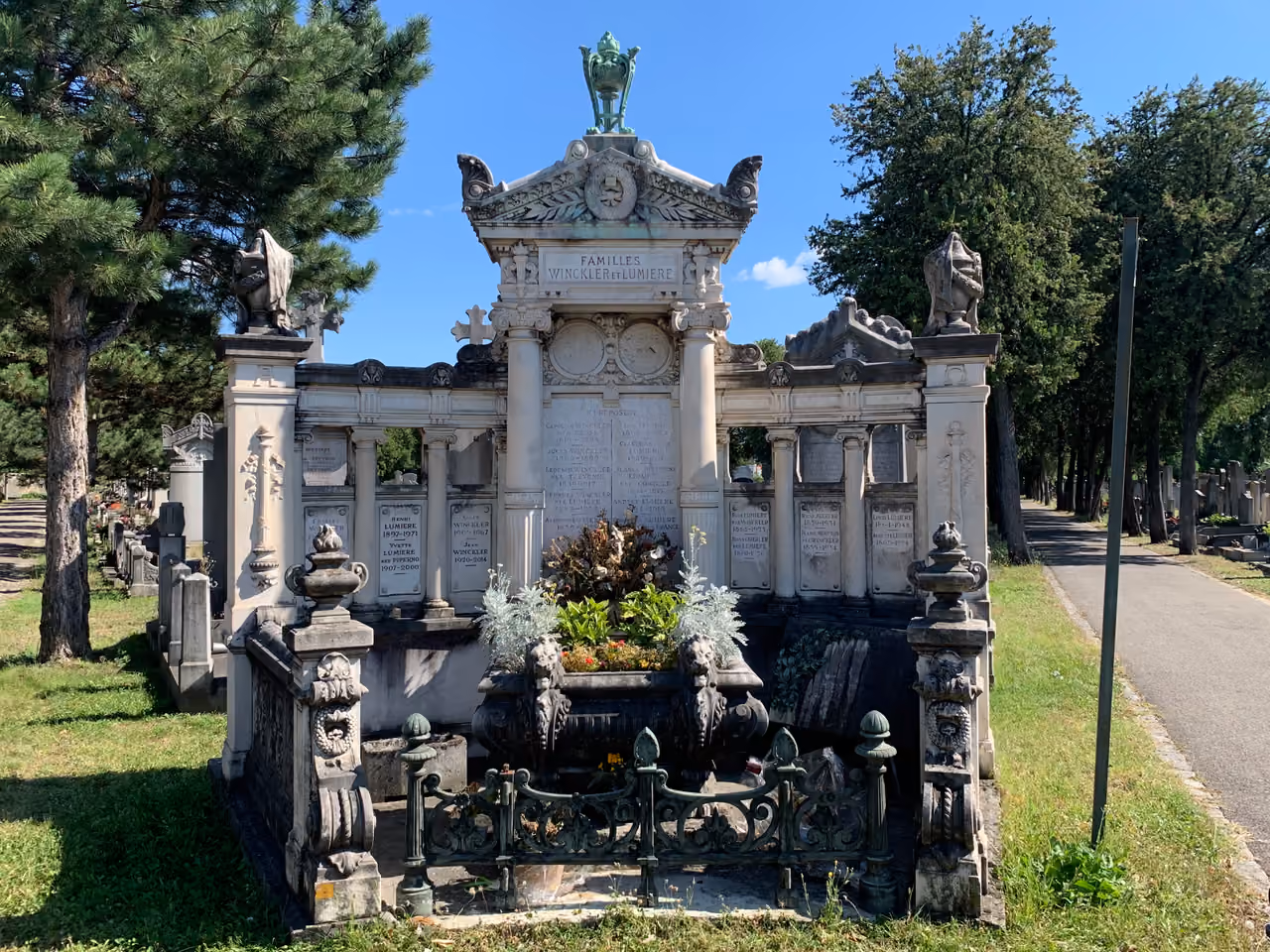 The tomb of the Lumiere brothers at the Guillotiere Cemetery featuring an ornate stone monument with columns and a decorative planter