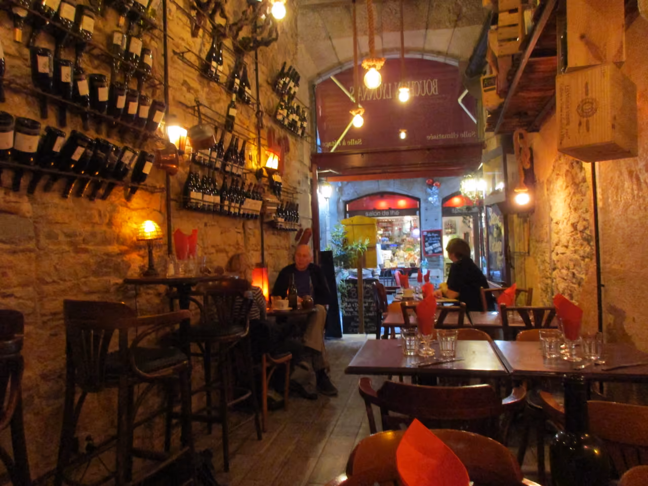 Alt Tag: Cozy traditional wine bar interior with stone walls, wooden tables and shelves filled with wine bottles in the historic Saint-Jean quarter