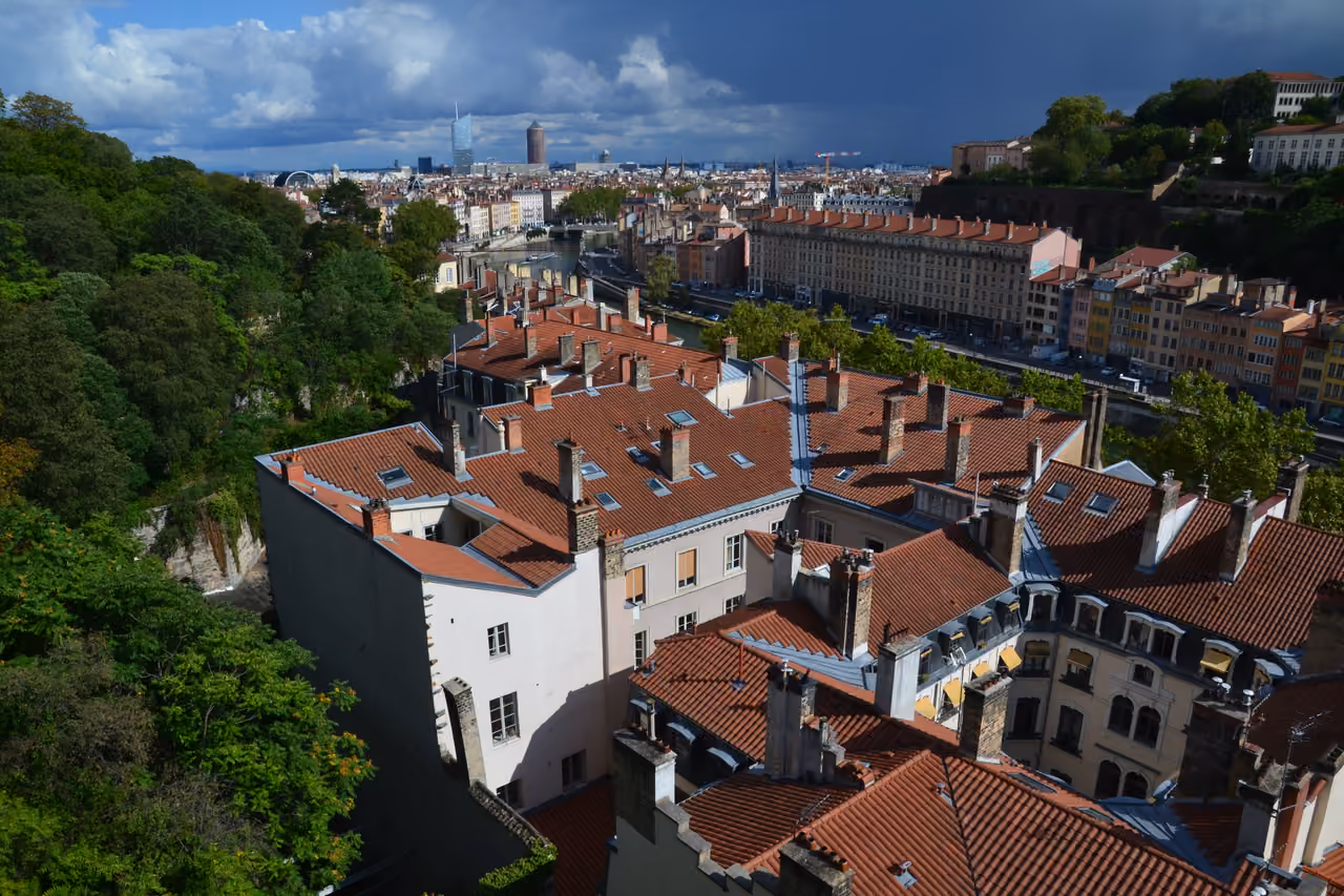 Panoramic view of historic terracotta rooftops and distant modern skyscrapers from a lush green park
