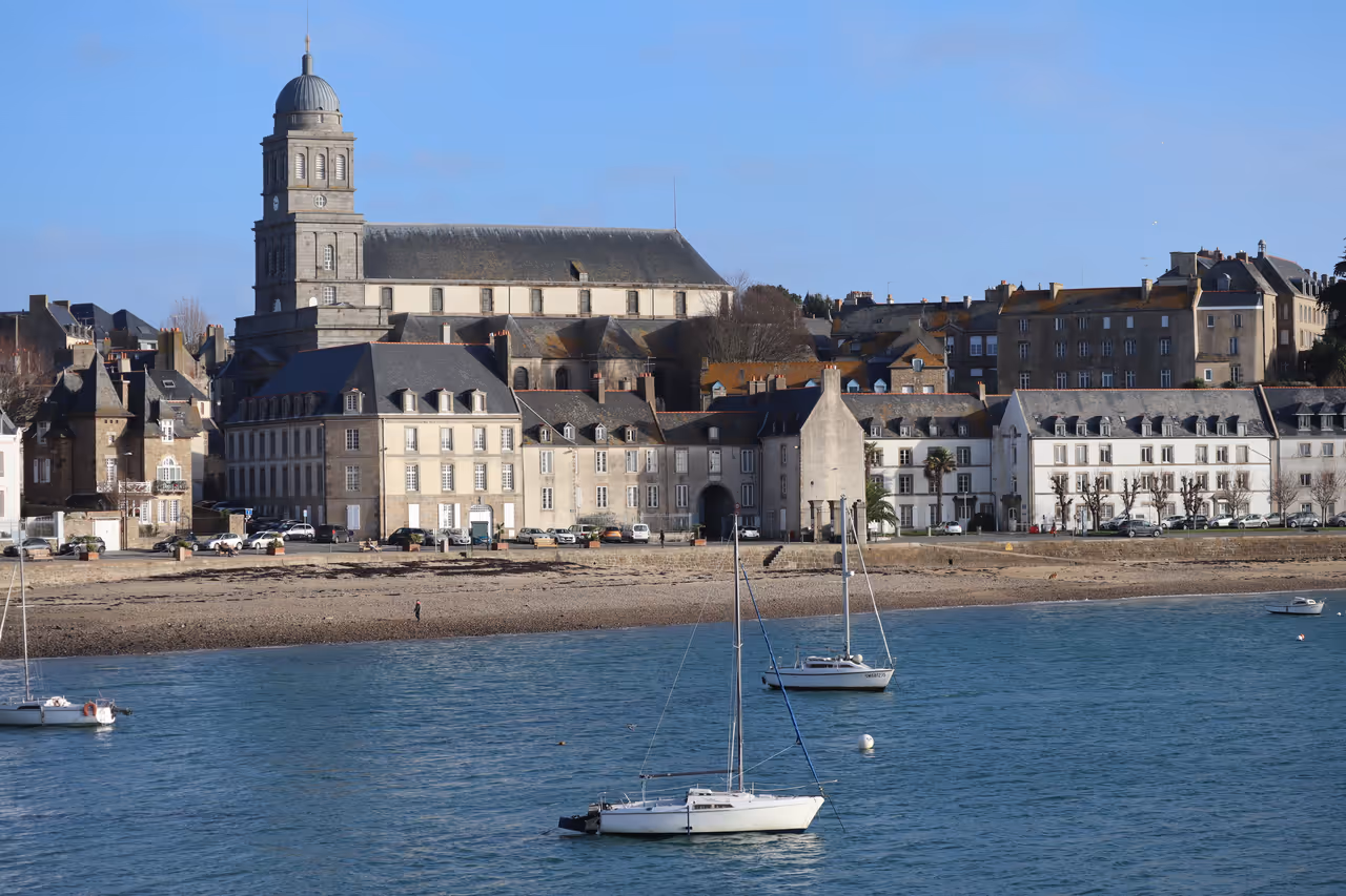 Historic stone façade and tower of Holy Cross Church overlooking sailboats anchored in the estuary at Saint-Malo Brittany
