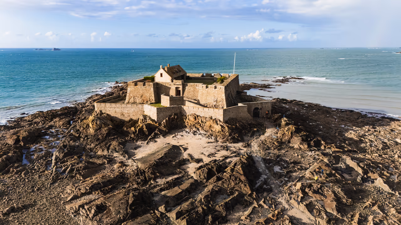 Aerial view of Fort National on a rocky tidal island in Saint-Malo with historic stone walls surrounded by the turquoise ocean under a blue sky