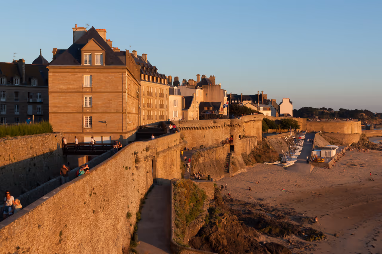 Stone ramparts of the fortified city of Saint-Malo leading to Tour Bidouane with historic granite buildings and a sandy beach