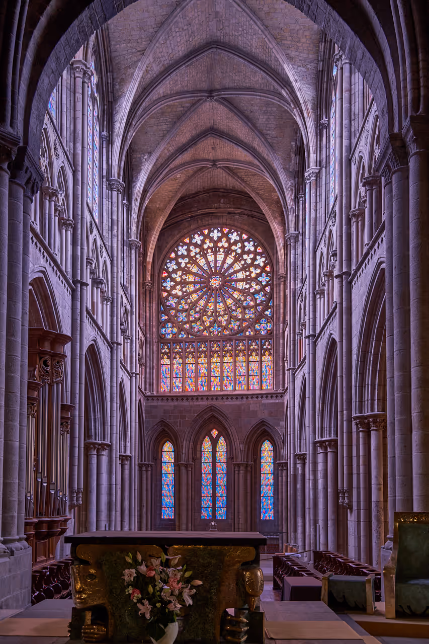 Interior view of the Saint-Vincent Cathedral of Saint-Malo showcasing gothic stone vaulting, columns, and a prominent stained-glass rose window above the altar