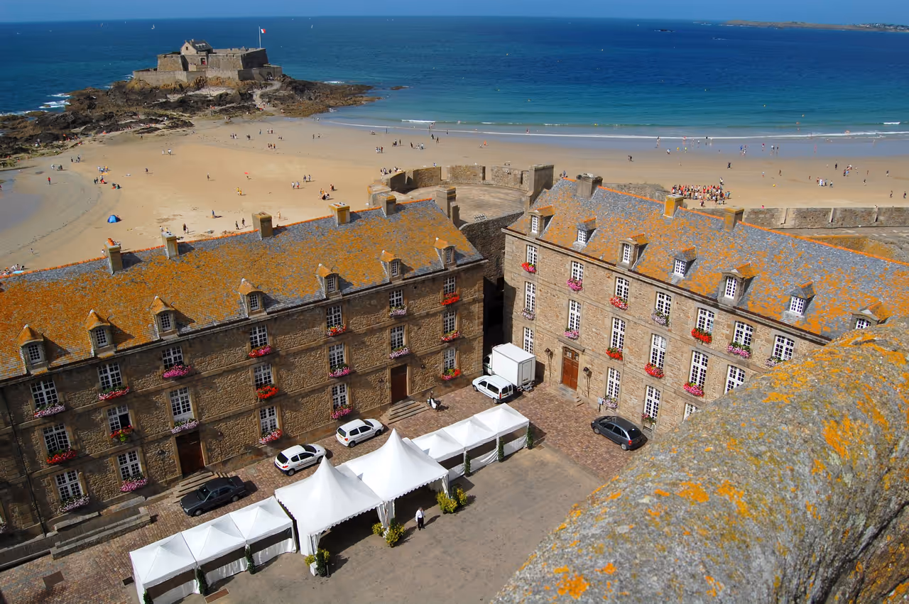 Château ducal de Saint-Malo with its historic stone façade, flower-filled windows, and views over the sandy beach and blue waters of the Atlantic