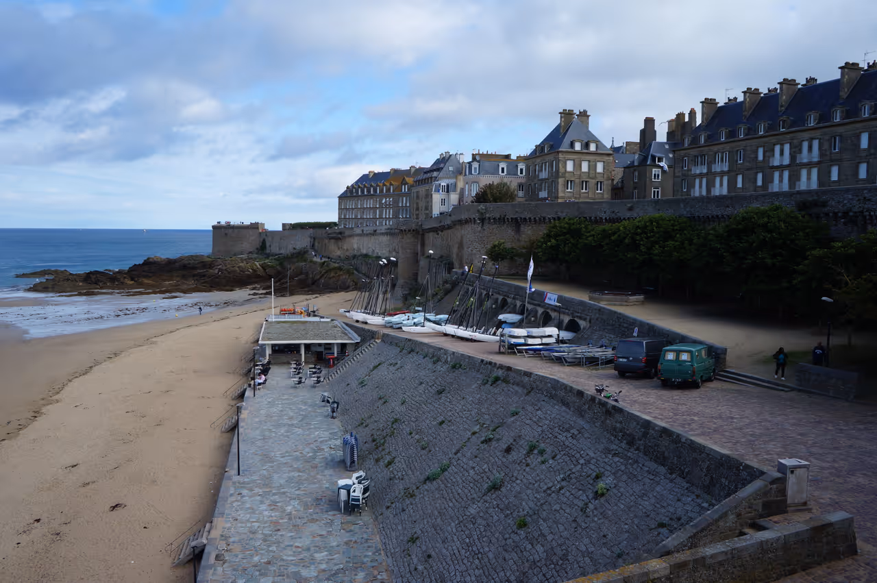 Stone ramparts of the fortified city of Saint-Malo leading to Tour Bidouane with historic granite buildings, a sandy beach, and views over the ocean