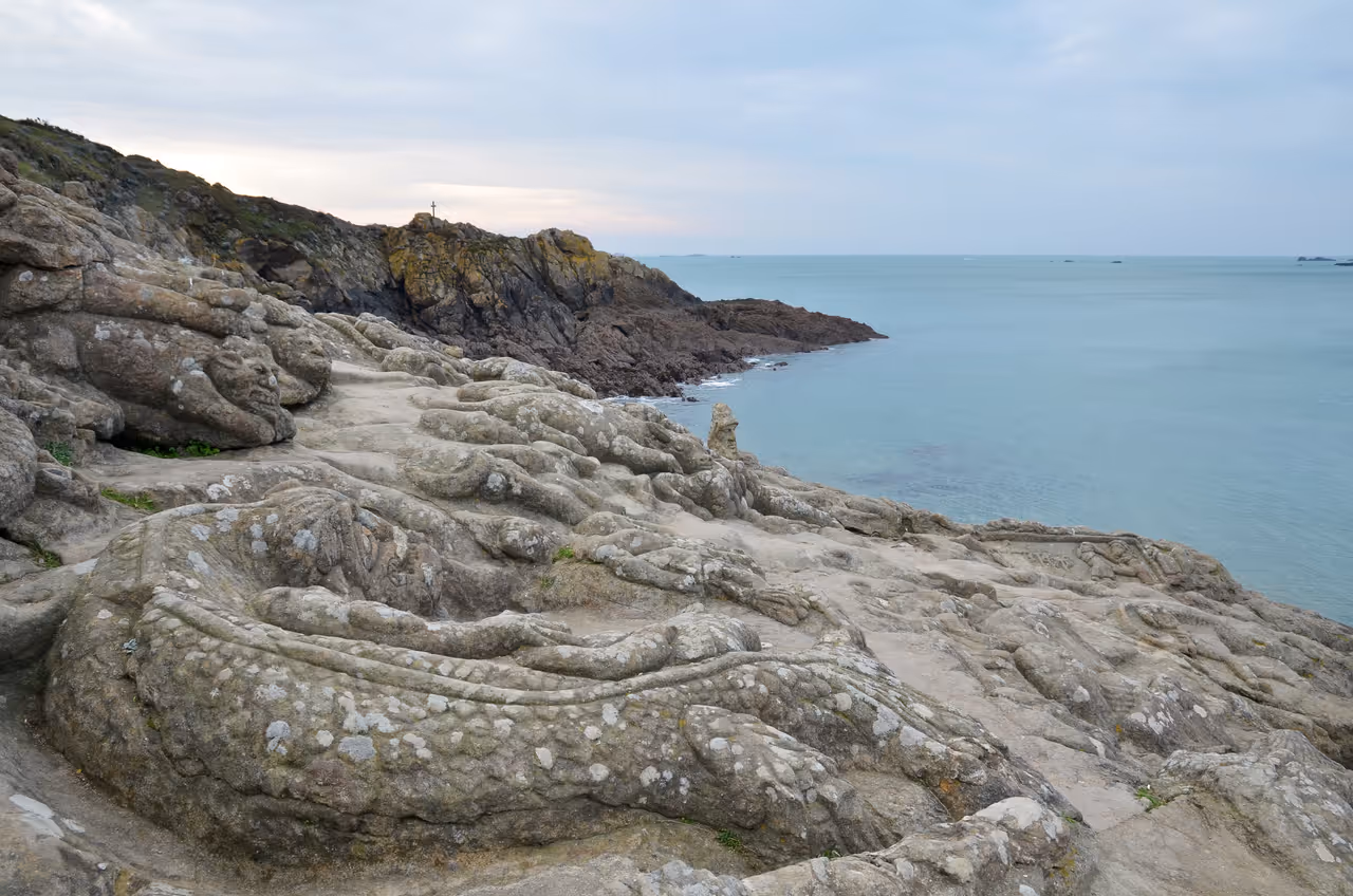 Sculpted granite faces of Rochers sculptés de Rothéneuf carved into the coastal rocks along the blue ocean water in Brittany