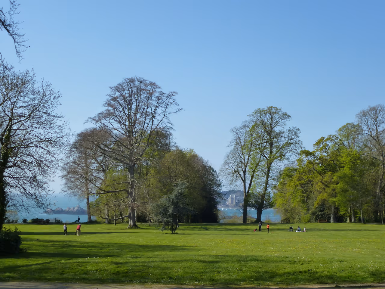 Lush green lawn and towering mature trees of the Grand Park of La Briantais overlooking the emerald waters of the Rance estuary near Saint-Malo