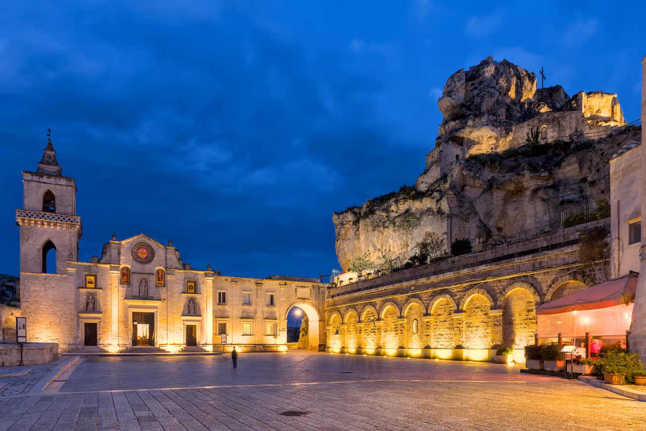 Piazza San Pietro Caveoso, with a church on the left and a rocky outcrop, after sunset, Matera