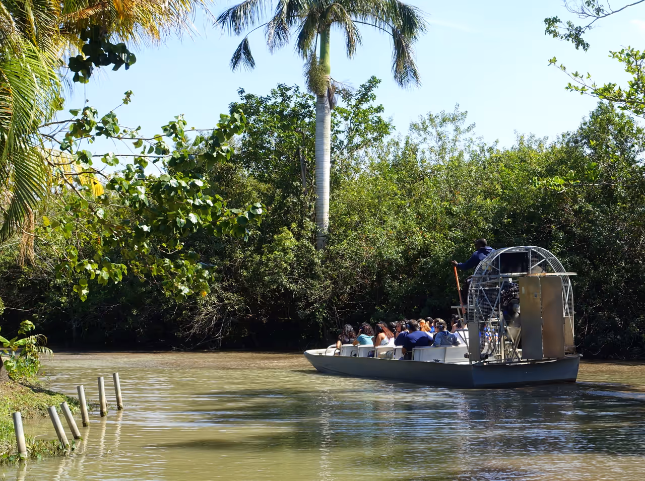 Tourists on an airboat gliding through a river surrounded by tropical trees at the Everglades Alligator Farm in Florida City, Florida