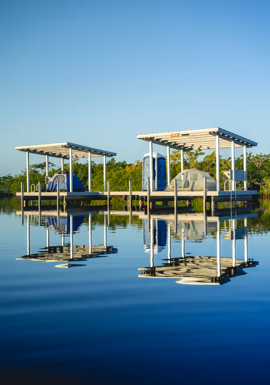 Two elevated wooden camping platforms with pitched tents reflecting on calm water in Everglades National Park