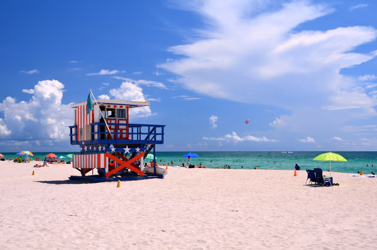 Patriotic red, white and blue lifeguard tower on a crowded sandy beach with turquoise water under a blue sky