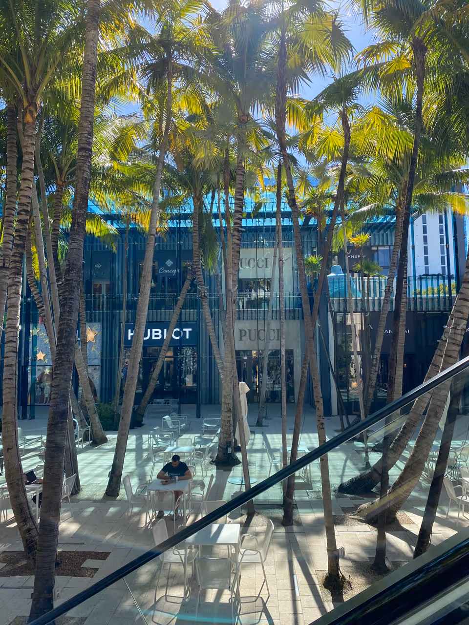 An outdoor shopping courtyard in the Miami Design District with palm trees, outdoor seating and luxury retail storefronts