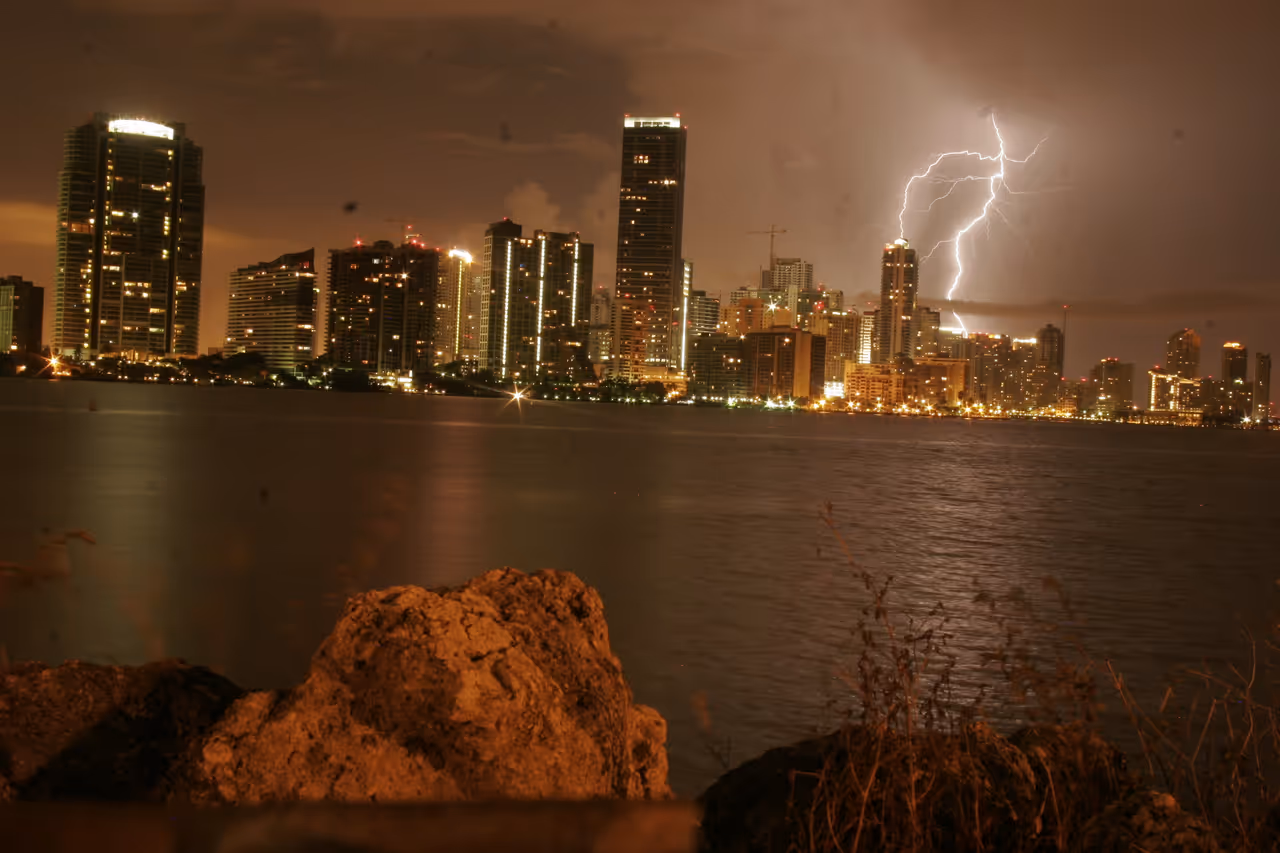Miami downtown skyline illuminated at night across the water during a dramatic thunderstorm with a bright lightning strike