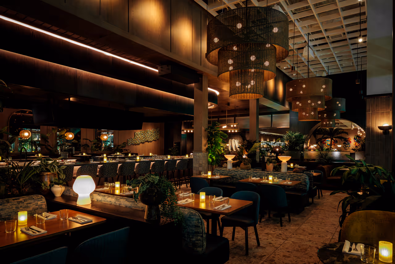 Dimly lit modern interior of Earls Kitchen and Bar at Miami Worldcenter in Florida featuring warm lighting, large woven chandeliers, wooden dining tables and plush seating