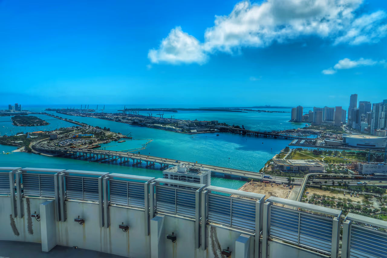 Aerial panorama of the Miami harbour showing turquoise waters, bridges and the city skyline under a blue sky with scattered clouds