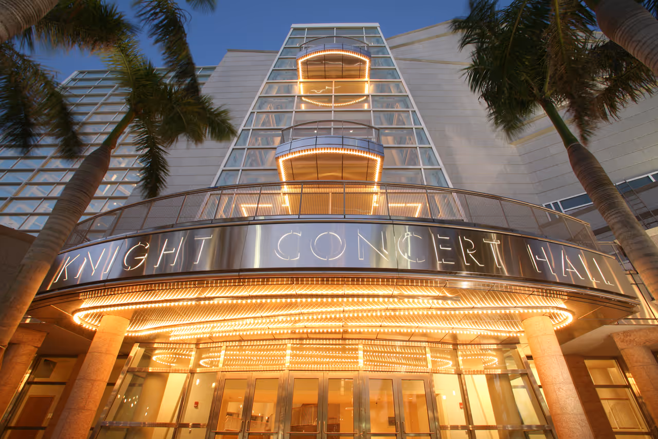 Exterior of the illuminated Knight Concert Hall at the Adrienne Arsht Center for the Performing Arts in Miami, Florida at dusk, framed by palm trees
