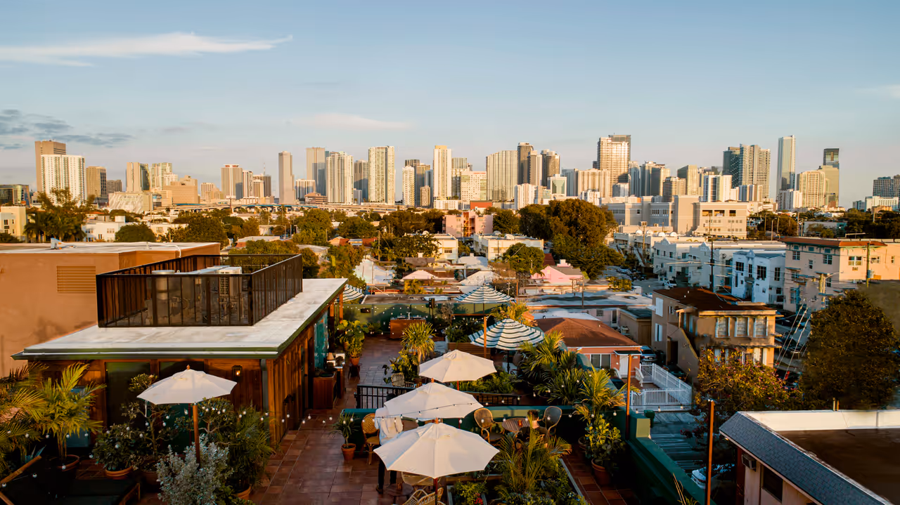 Scenic rooftop terrace in Little Havana with white umbrellas and lush green plants overlooking the Miami skyline at sunset