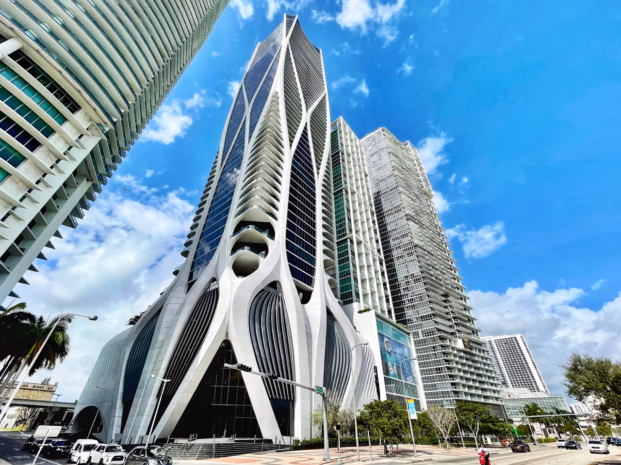 The striking futuristic exterior of the One Thousand Museum skyscraper designed by Zaha Hadid in Miami, featuring its iconic curved white exoskeleton against a clear blue sky