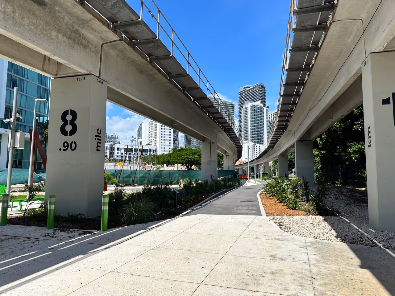 Paved pedestrian and cycle path of The Underline linear park in Miami winding beneath elevated railway tracks towards downtown skyscrapers