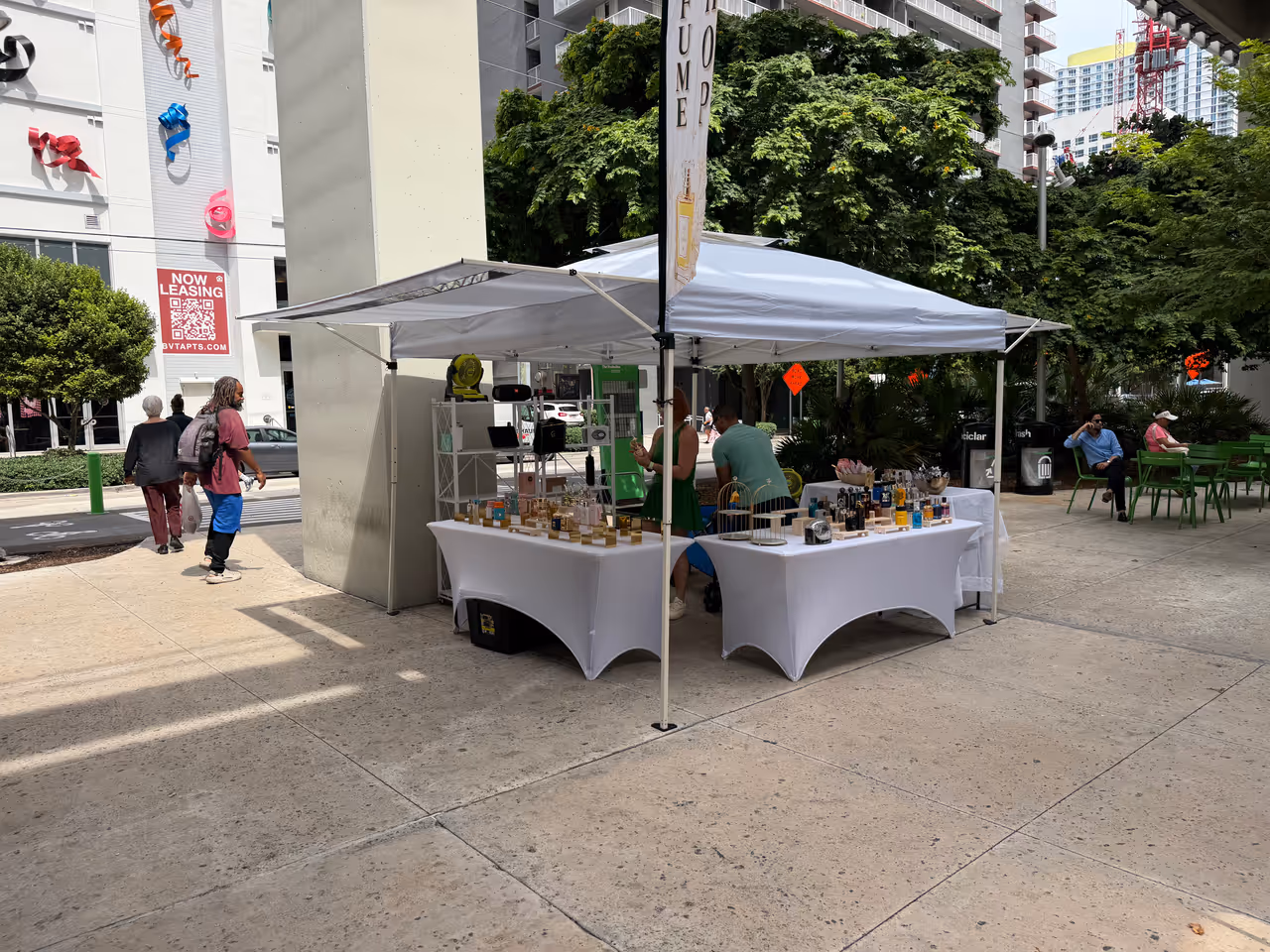 An outdoor farmers market stall with white canopies and tables displaying artisanal products under the Brickell Underline in Miami, Florida