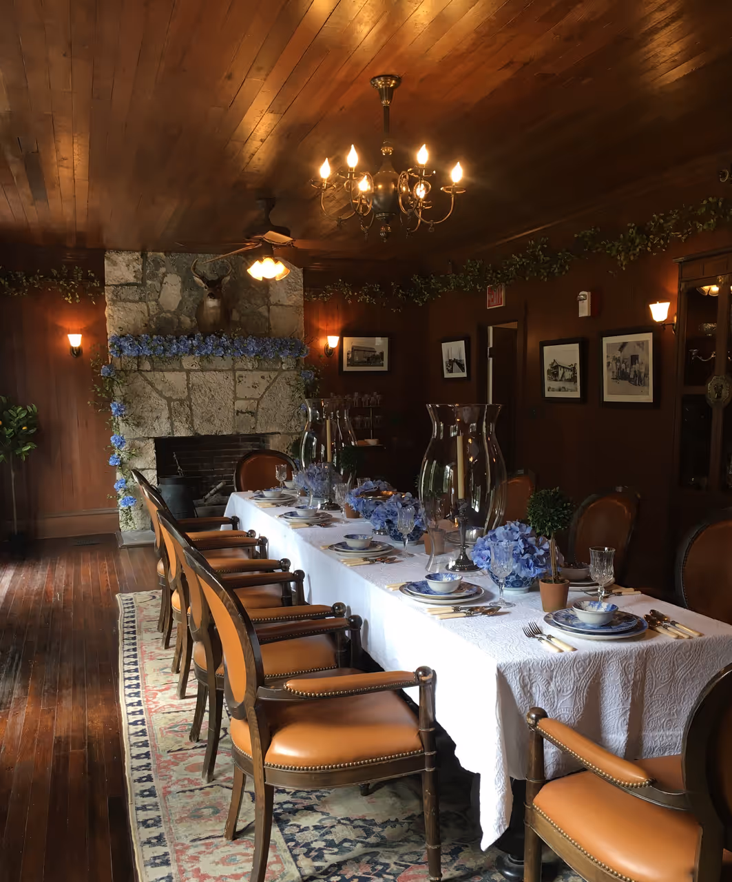 Elegant dining room with a long laid table, wooden chairs, a stone fireplace, and wood-panelled walls in the Stone House tavern