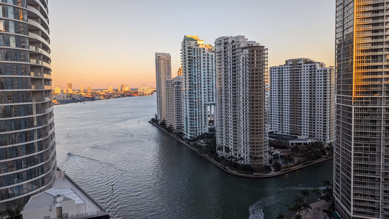 Aerial panoramic view of high-rise skyscrapers and luxury apartment buildings lining the waterfront channel in Brickell Key, Miami