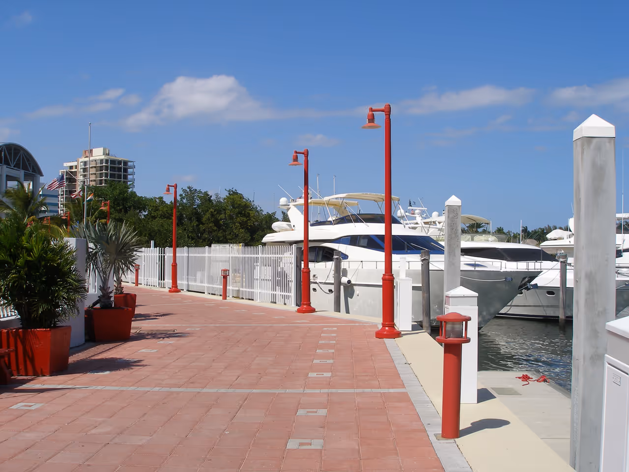 A brick walkway lined with red lampposts beside luxury yachts moored at Coconut Grove Marina