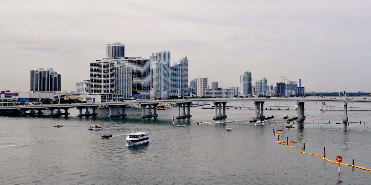 Panoramic view of the Miami skyline across Biscayne Bay showing the Mac Arthur Causeway bridge, high-rise buildings, and boats on the water in Florida