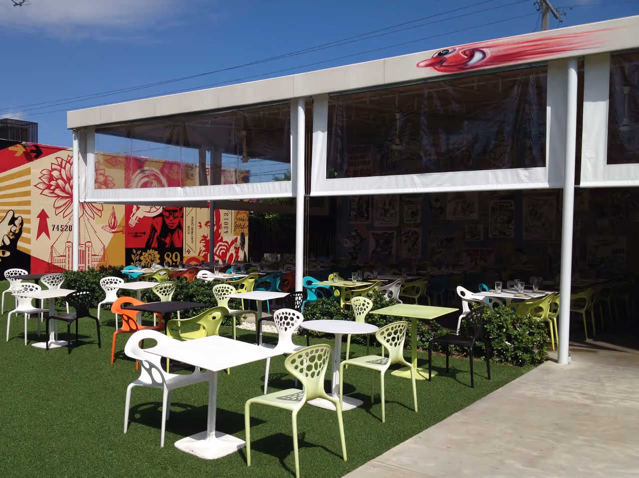 Outdoor restaurant seating area with colourful tables and chairs on artificial grass at Wynwood Walls in Miami, featuring vibrant murals and a white canopy awning