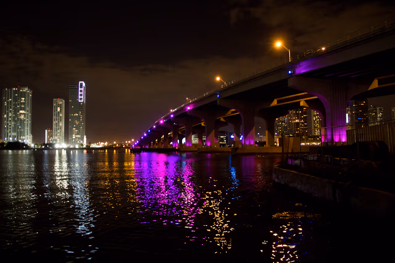 MacArthur Causeway in Miami at night with purple illuminated bridge lights and city skyline reflections on the water