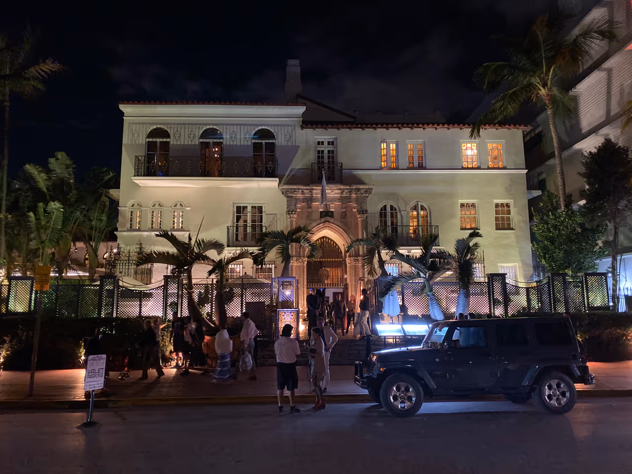 The facade of the historic Versace Mansion lit up at night with palm trees and a car on Ocean Drive in Miami Beach, Florida